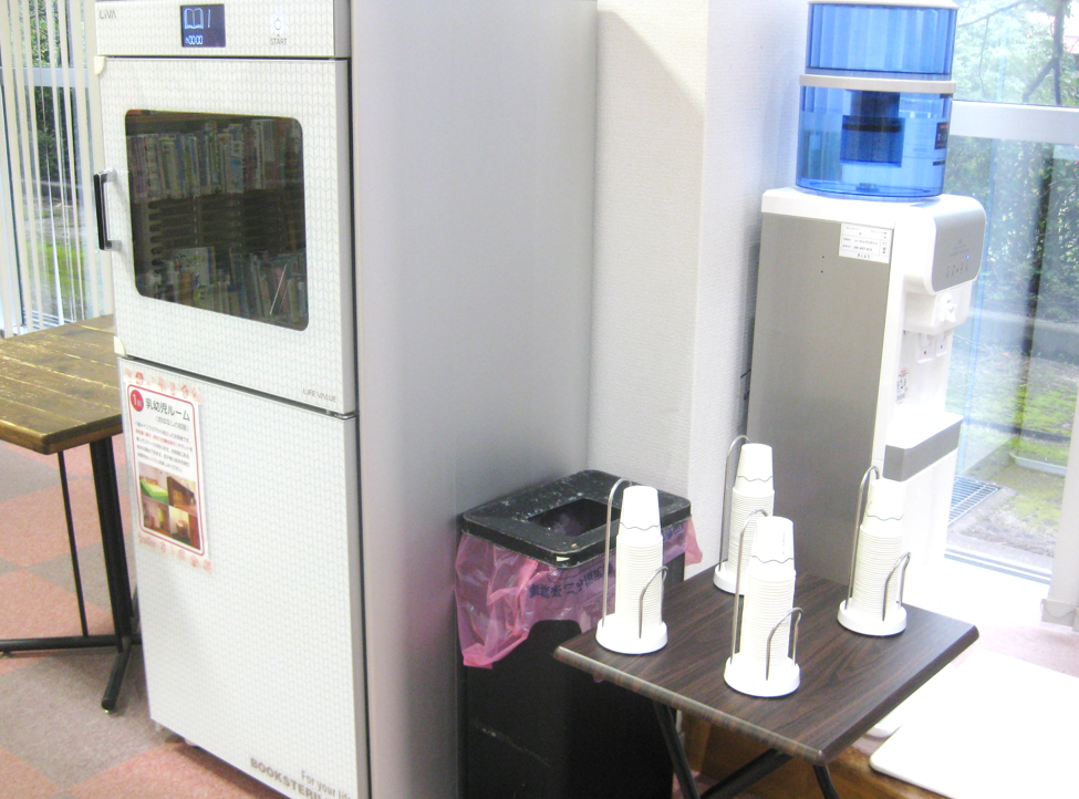 左から図書除菌機、ゴミ箱、紙コップが載った机、冷水器